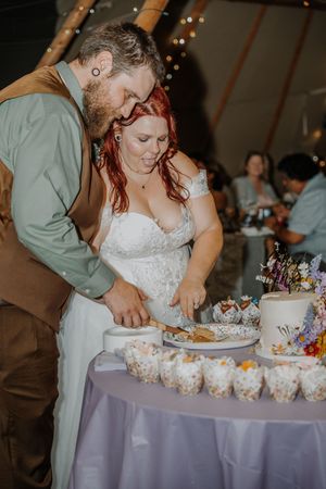 Newlyweds cut their wedding cake together at a reception inside a decorated teepee venue.
