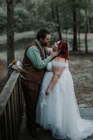 Bride and groom share a romantic moment on a wooden bridge surrounded by lush forest greenery.