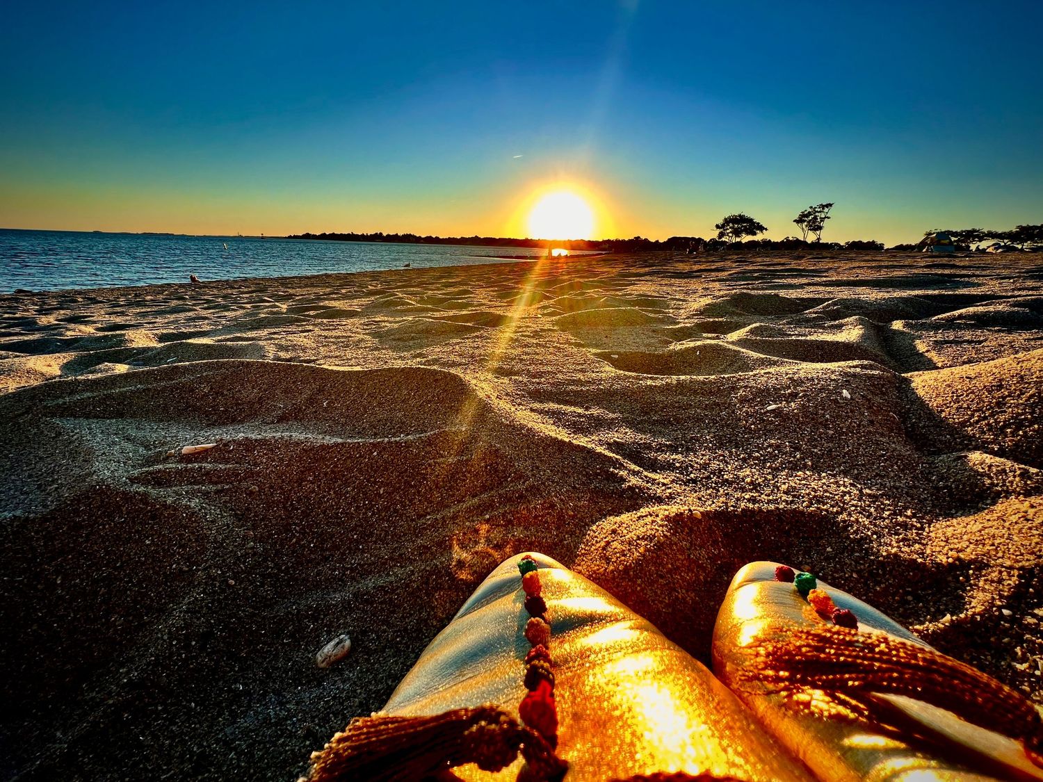 A golden sunset casts warm light over sandy beach with a colorful kayak in the foreground and calm ocean waters.
