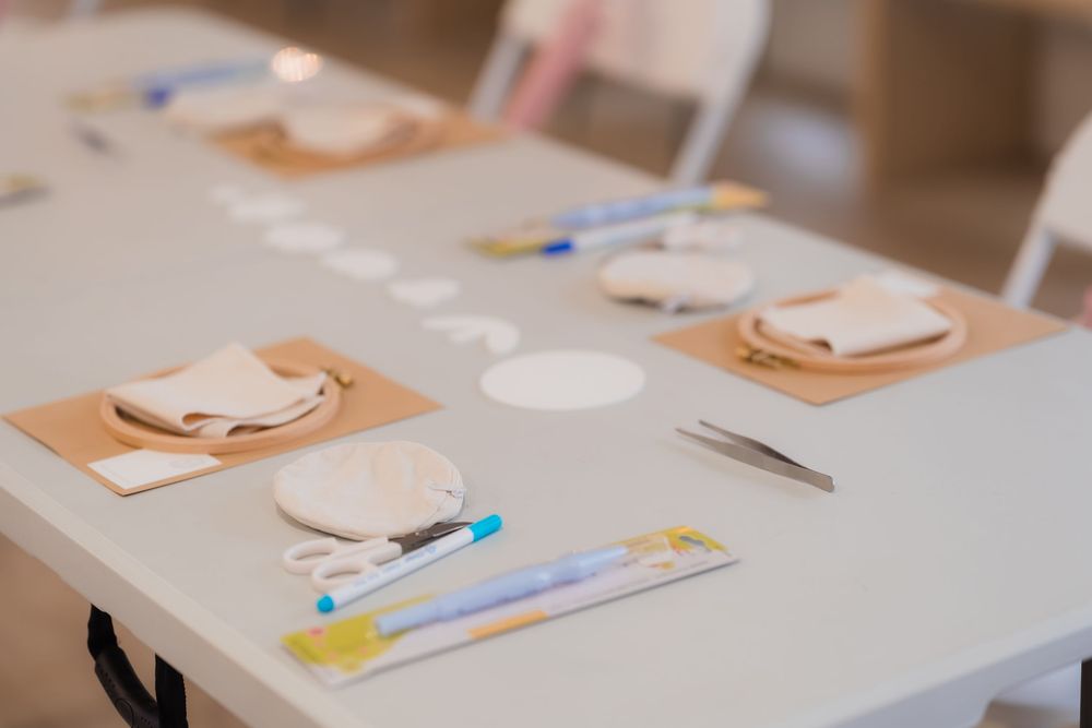 Craft workshop table setup with clay discs, tweezers, markers, and supplies on cork mats.
