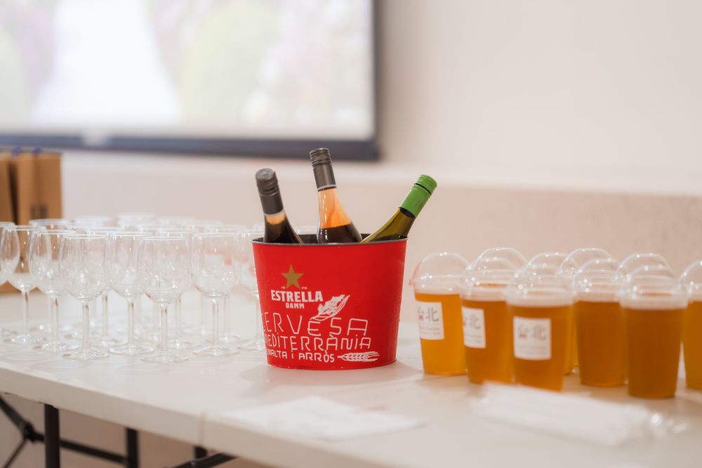 Red Estrella Damm ice bucket with wine bottles surrounded by beer glasses and champagne flutes on a white table.