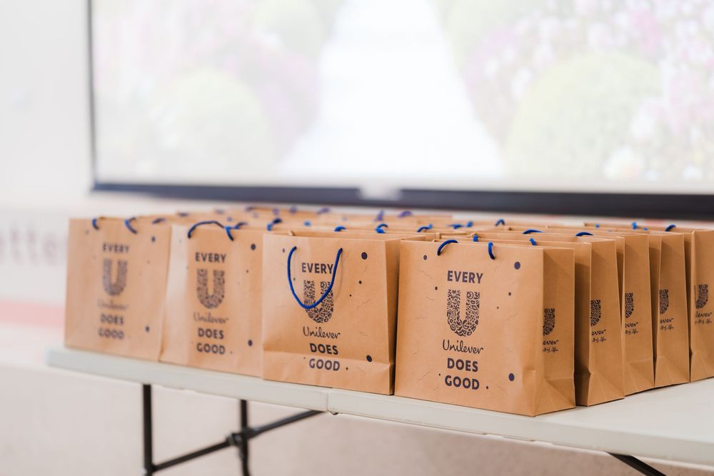 Kraft paper Unilever gift bags with Every U Does Good branding arranged on a white table.