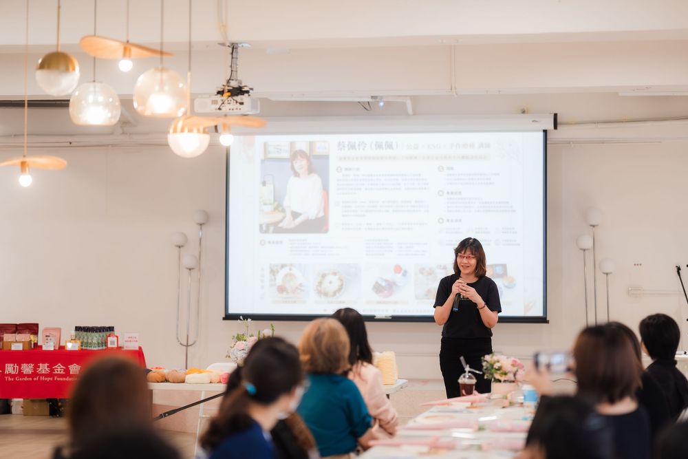 Woman presenting at a seminar with a projector screen displaying a profile, attendees seated at tables in a modern venue.