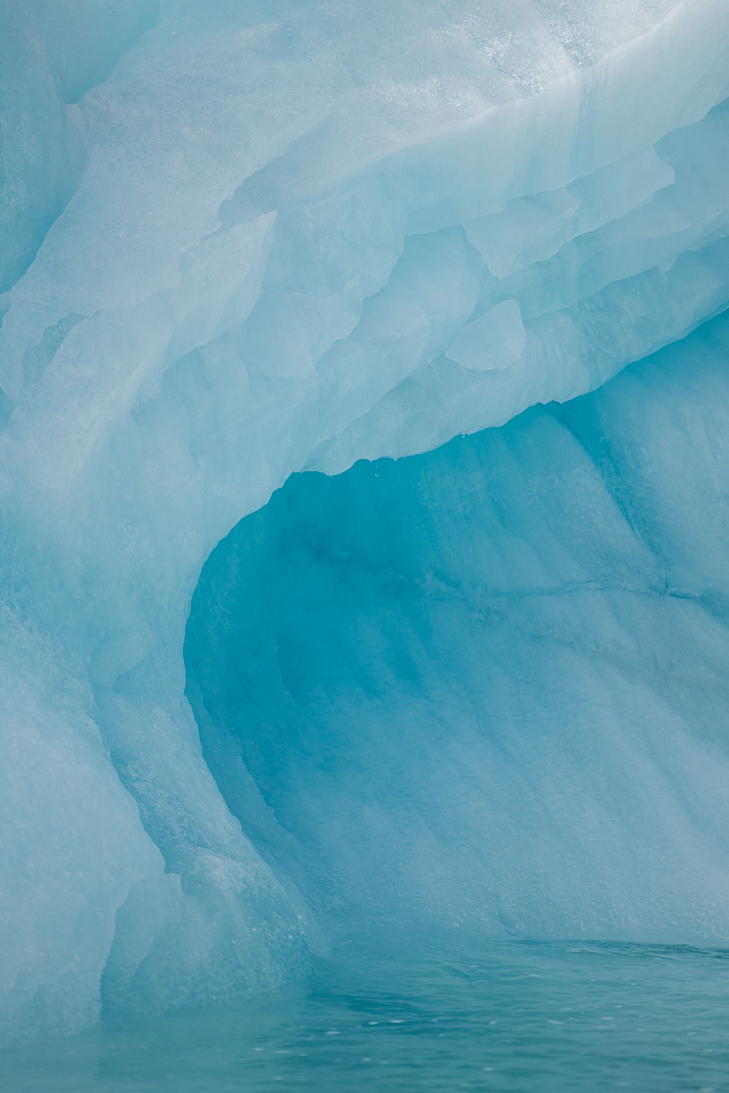 Courbe bleu profond creusée dans la glace claire d'un iceberg, en cadrage serré