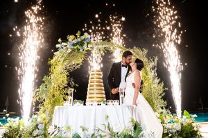 A panoramic view of a wedding ceremony with sparklers and pyrotechnics illuminating an outdoor evening celebration.