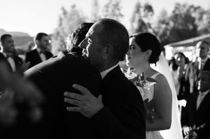 Black and white wedding photo showing an emotional embrace during an outdoor ceremony with guests watching in the background.