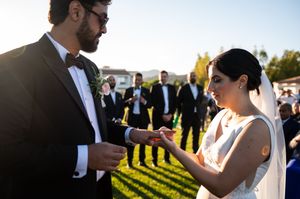 Newlywed couple shares an intimate moment during sunset at an outdoor wedding reception with guests in background.