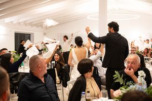Wedding guests raise their hands in celebration during a joyous reception in a bright white venue.