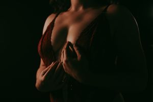 Woman in red lingerie posing in dramatic low-key lighting against dark background.