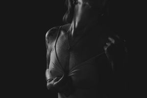 Black and white photo of a fit person in a wet white shirt, dramatically lit against a dark background.