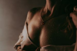 Close-up of a woman's bare back and shoulder with a delicate gold necklace in warm, moody lighting.