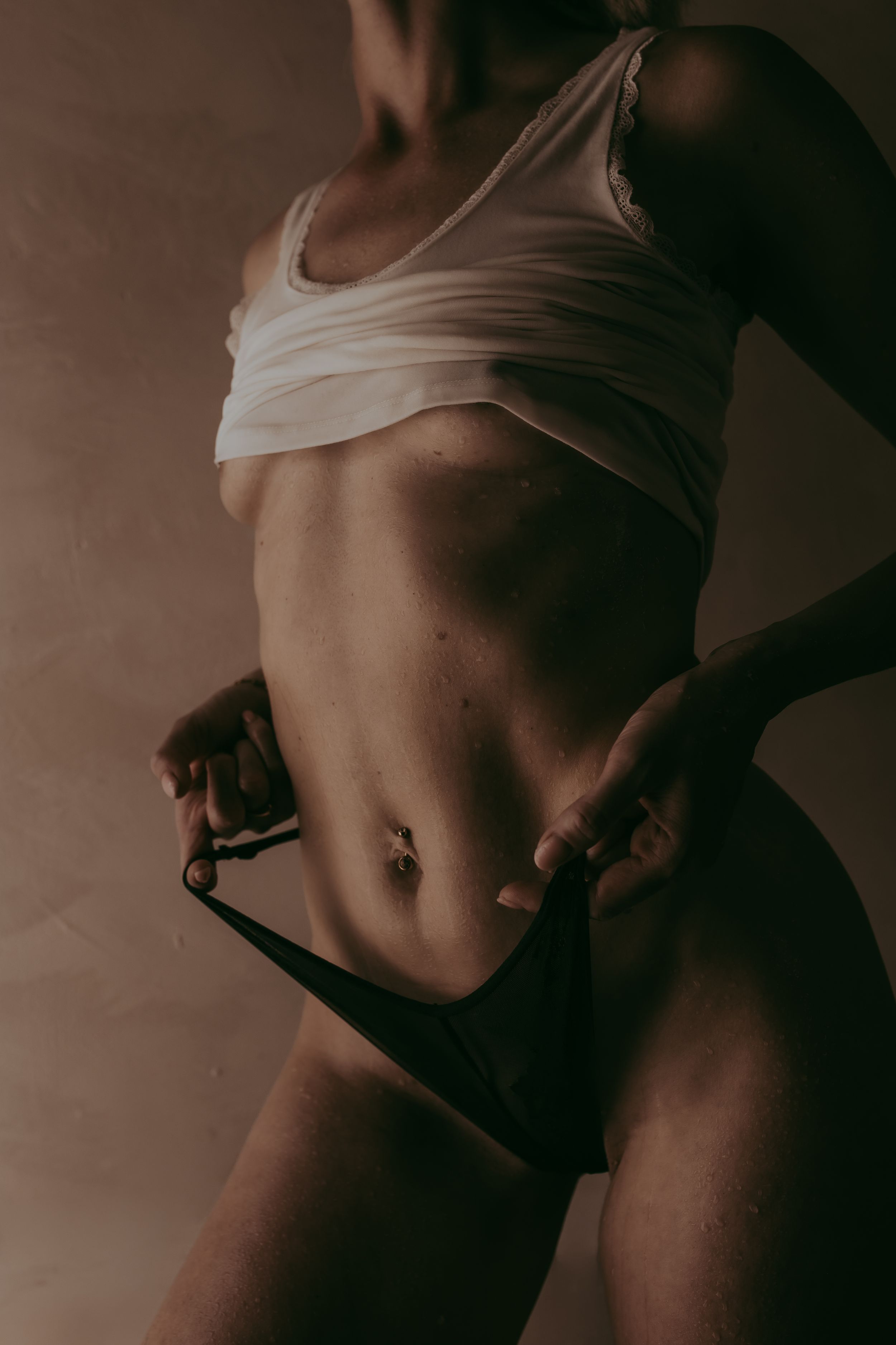 Close-up of a toned female torso in a white crop top and black bikini bottoms against a warm brown background.