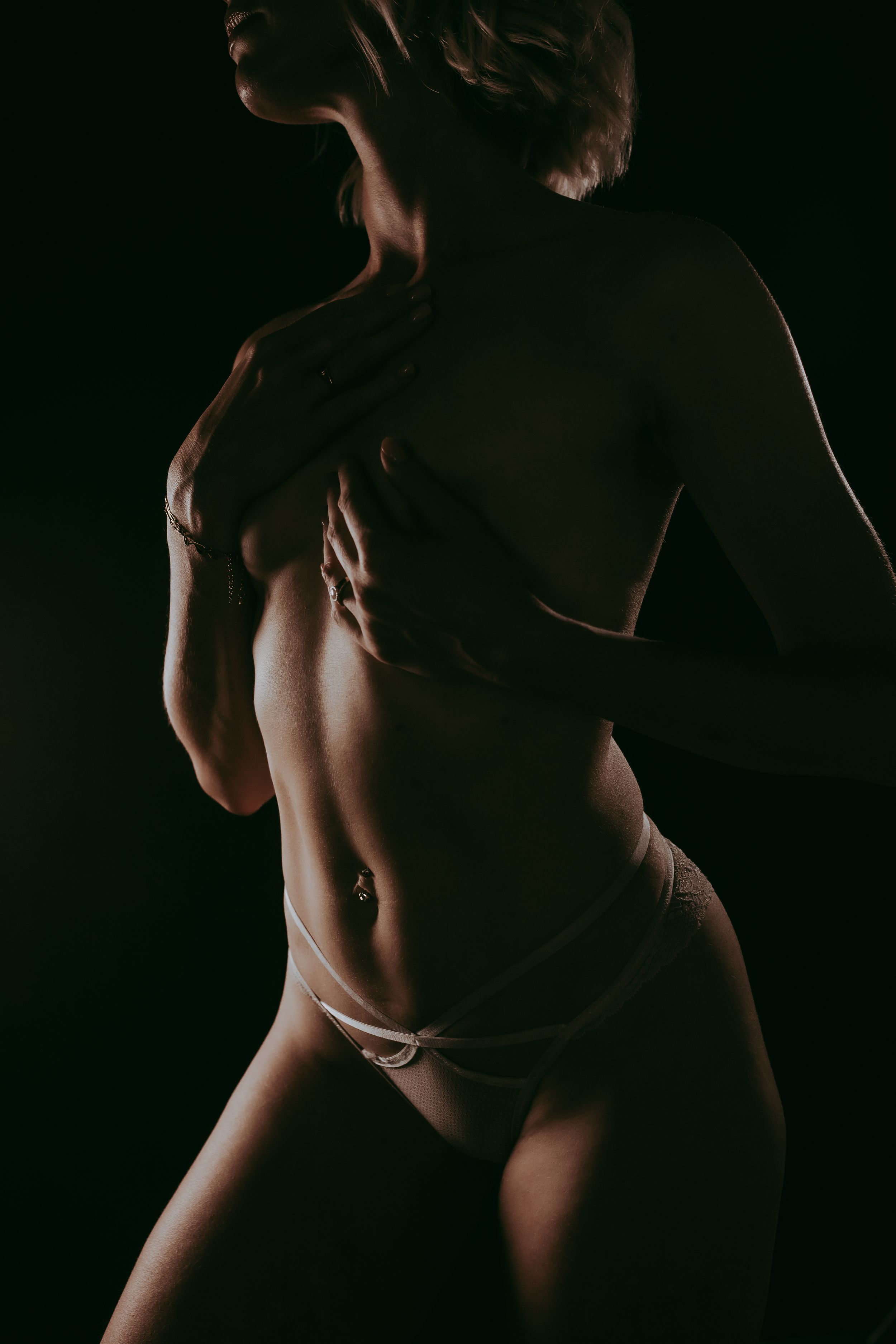 Artistic low-key studio photograph of a woman in white underwear posed against a dark background.