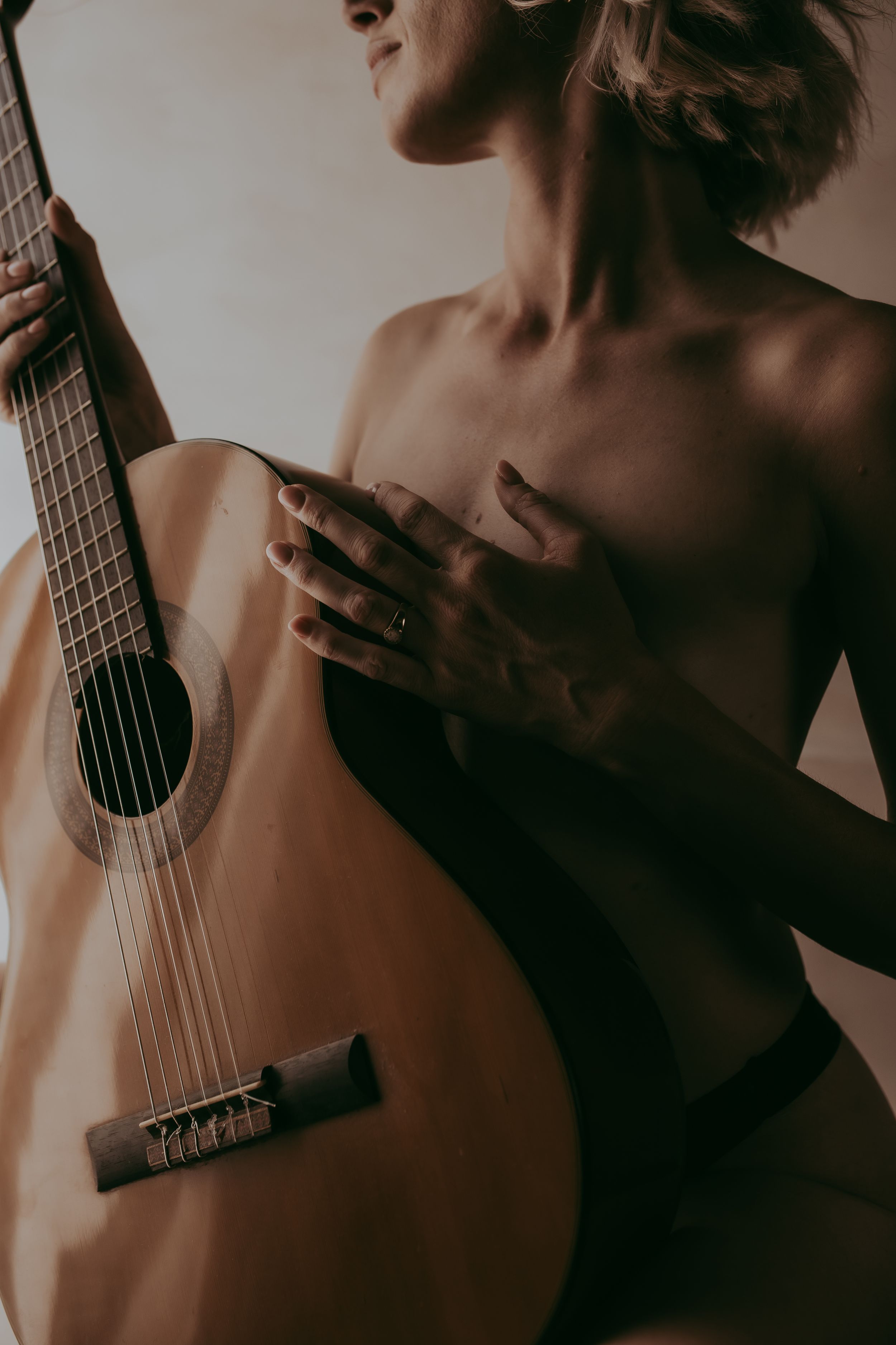 A woman holds an acoustic guitar close to her body in a moody, artistic portrait with warm tones.