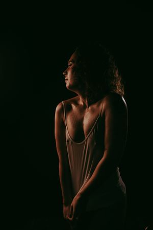 A woman in a low-cut tank top poses against a dark background in dramatic low-key studio lighting.