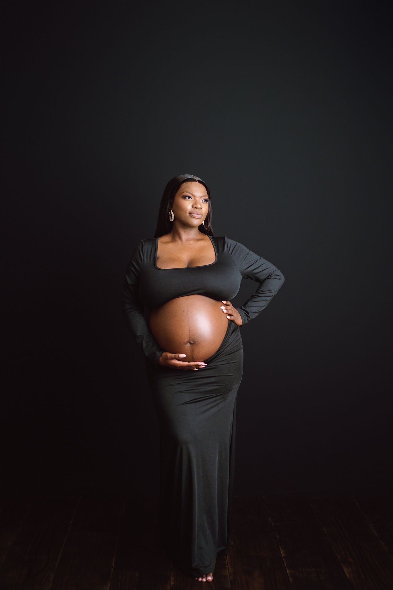Studio maternity portrait of expecting mother wearing an elegant dress against a black backdrop