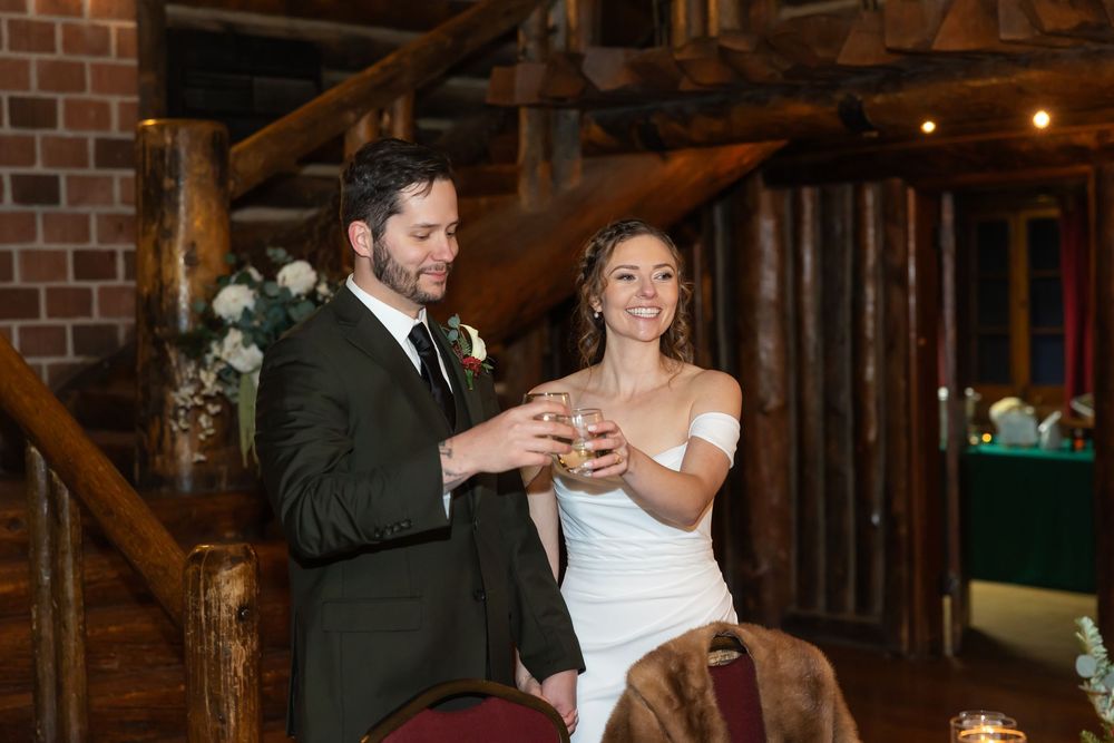 Bride and groom toasting with champagne glasses at rustic log cabin wedding reception venue.