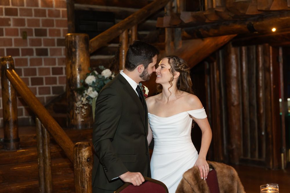 Couple sharing a romantic kiss in a rustic log cabin wedding venue with wooden staircase backdrop.