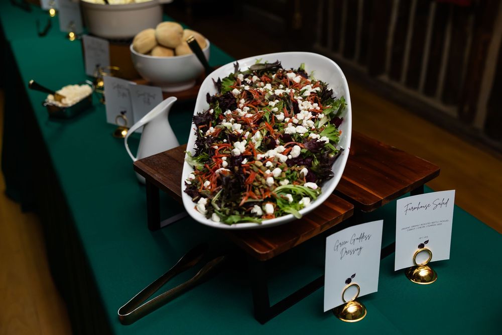 Elegant wedding reception salad buffet display on green tablecloth with white serving dish and menu cards.