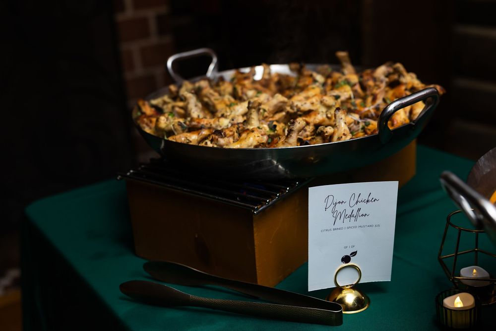 Golden buffet pan filled with Djon Chicken Makhani served on a green draped table at an elegant event.