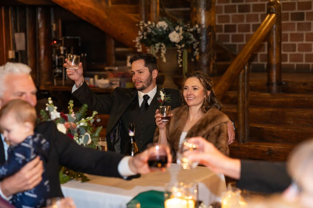 Bride and groom raising glasses during wedding toast in rustic barn venue with candlelit tables.
