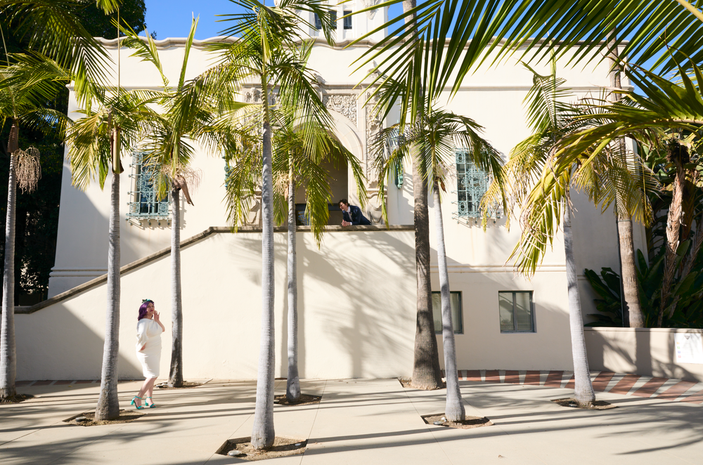White building exterior with tall palm trees casting shadows on a sunny day in a tropical setting.