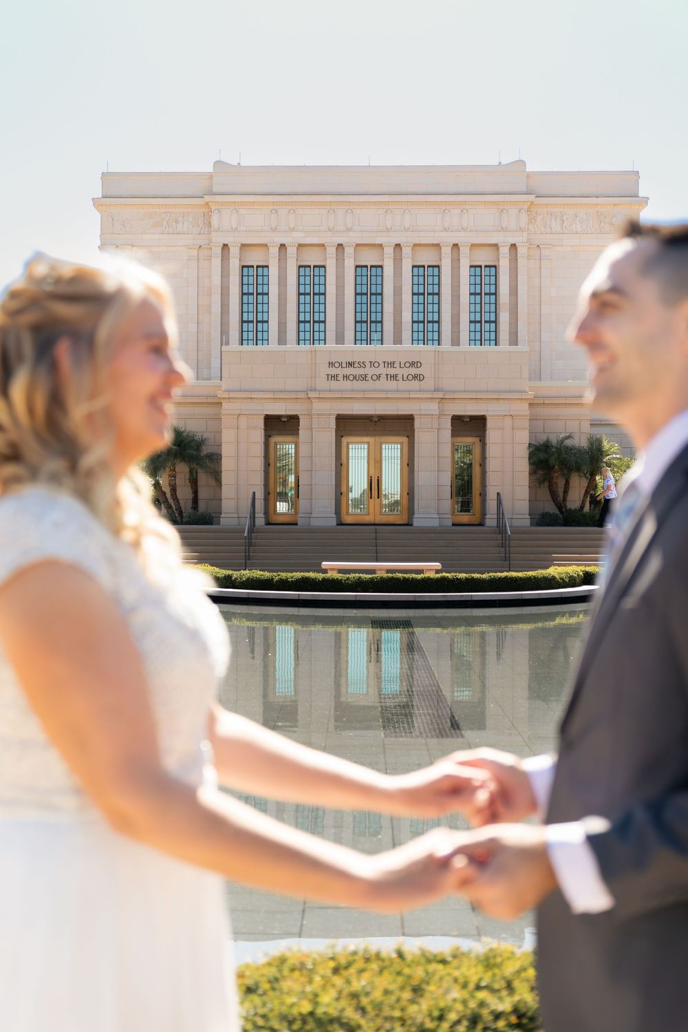 Bride and groom holding hands in front of an LDS temple reflecting pool on their wedding day.