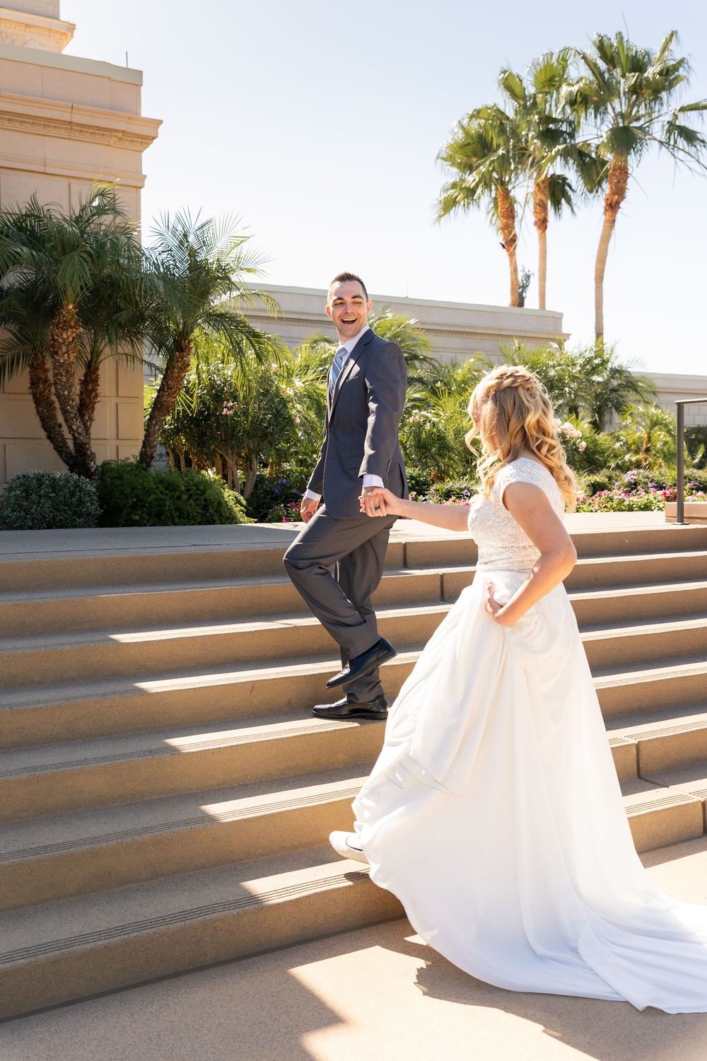 Bride and groom holding hands walking up stone steps with palm trees in background on their wedding day.