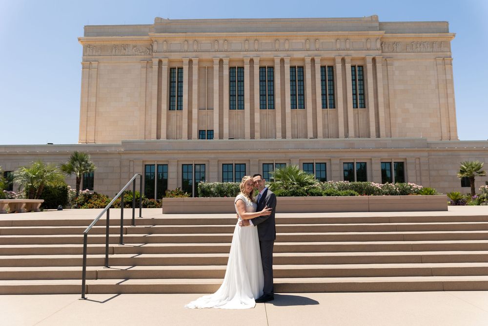 Bride and groom pose on steps outside a grand LDS temple on their sunny wedding day.