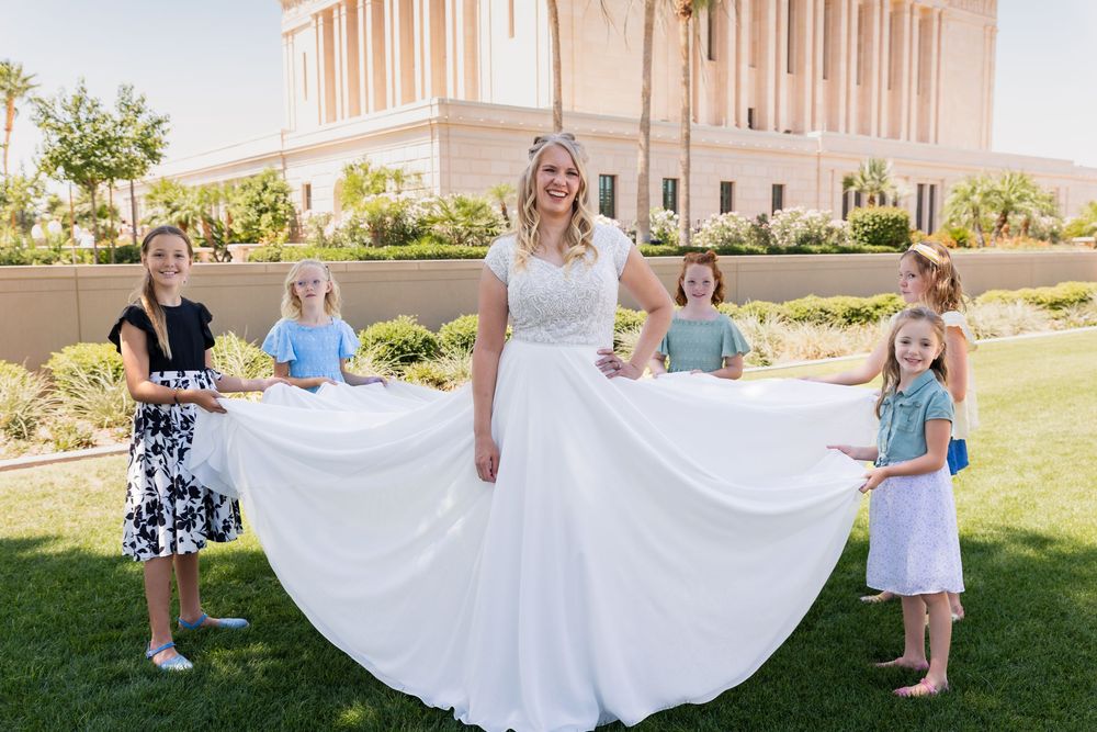 Bride in white wedding gown poses with young flower girls holding her skirt outside a temple.