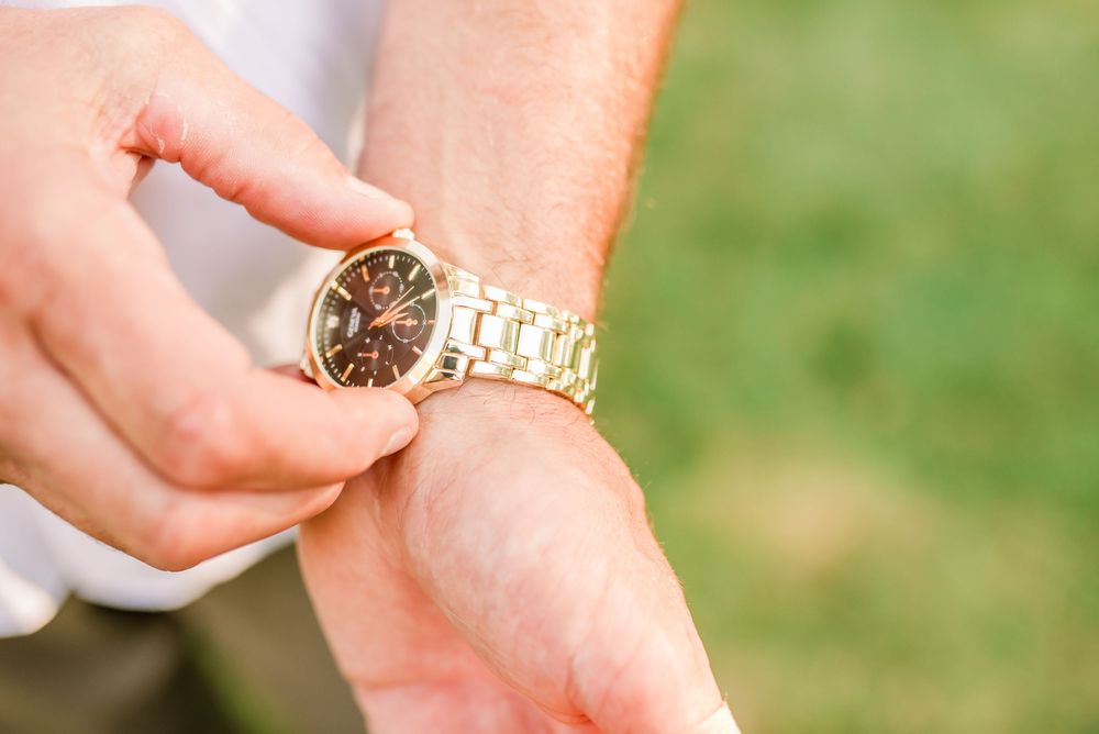Person adjusting a gold chronograph wristwatch on their wrist outdoors on a sunny day.