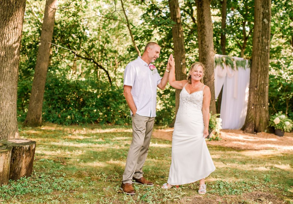 A joyful bride and groom hold hands and celebrate outdoors among trees after their wedding ceremony.