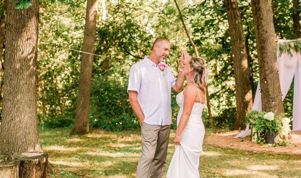 A bride and groom share a joyful moment outdoors surrounded by lush green trees during their wedding ceremony.