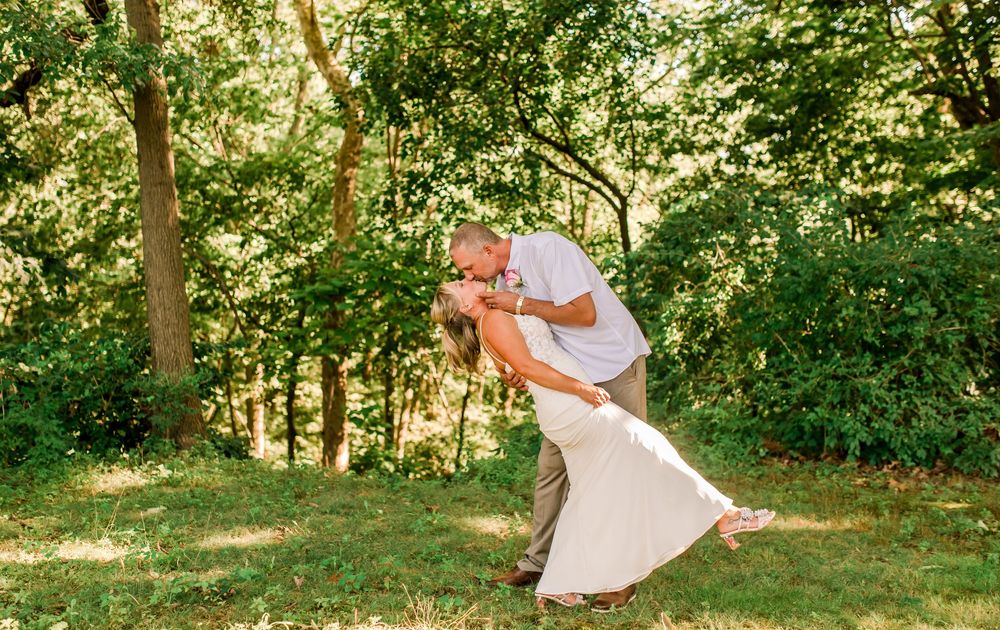 Couple sharing a romantic dip dance embrace outdoors in a lush green garden setting on their wedding day.