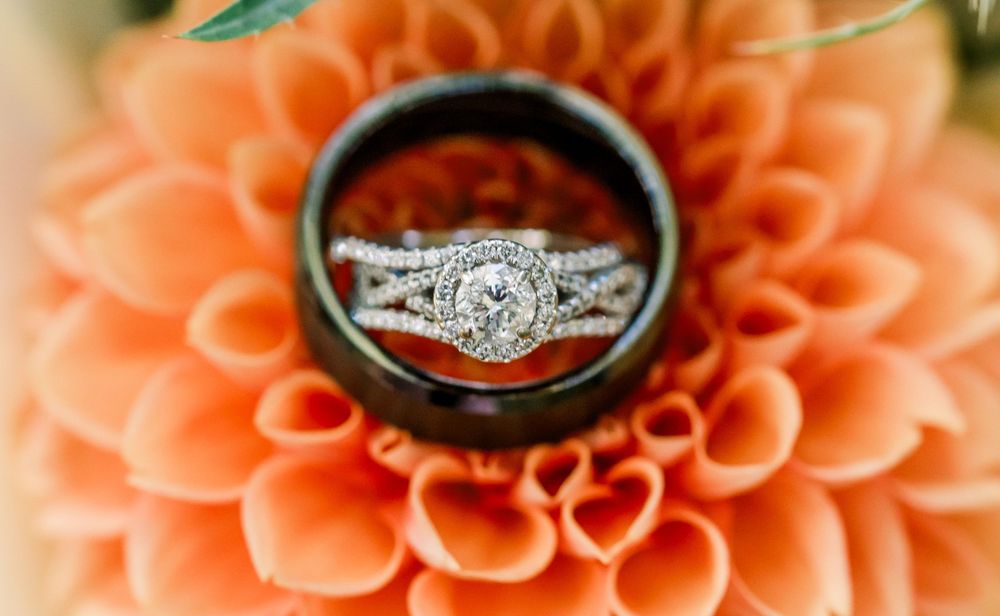Diamond halo engagement ring and wedding band set displayed on a peach dahlia flower.