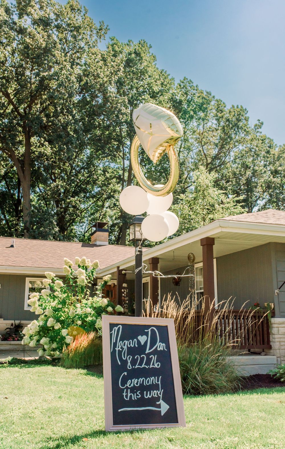 Outdoor wedding ceremony sign for Megan and Dan on 8.22.26 with ring balloon bouquet in front of a house.