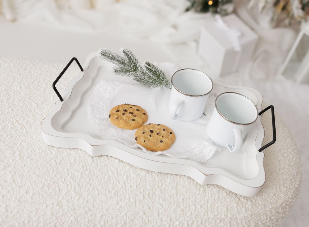 White decorative tray with chocolate chip cookies, two white mugs, and a pine sprig on a fluffy white surface.