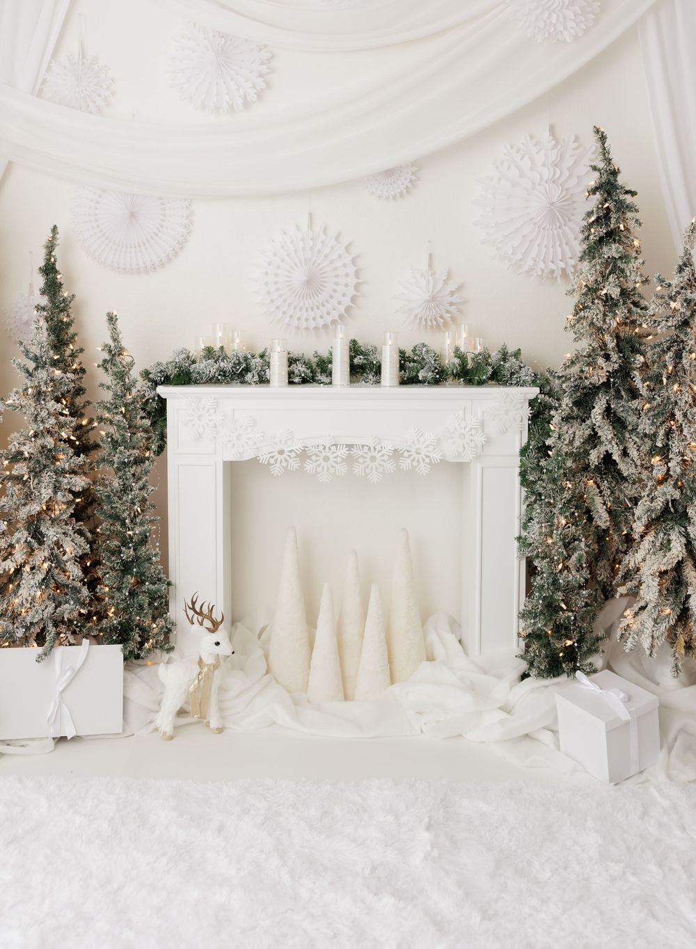 White Christmas fireplace scene with frosted trees, paper snowflakes, candles, and gift boxes in elegant winter decor.
