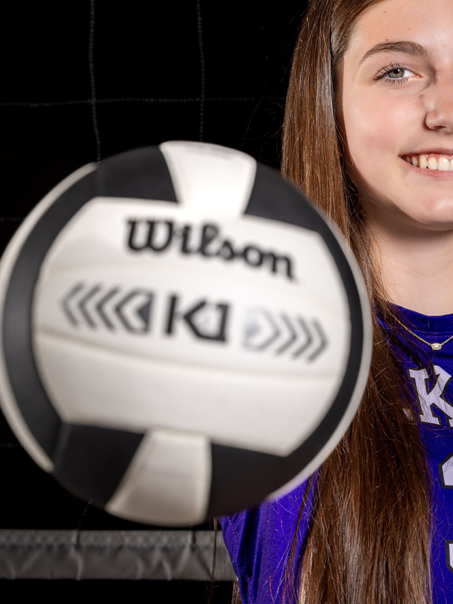Female basketball player in Elkins jersey poses smiling with multiple Wilson basketballs in a studio setting.