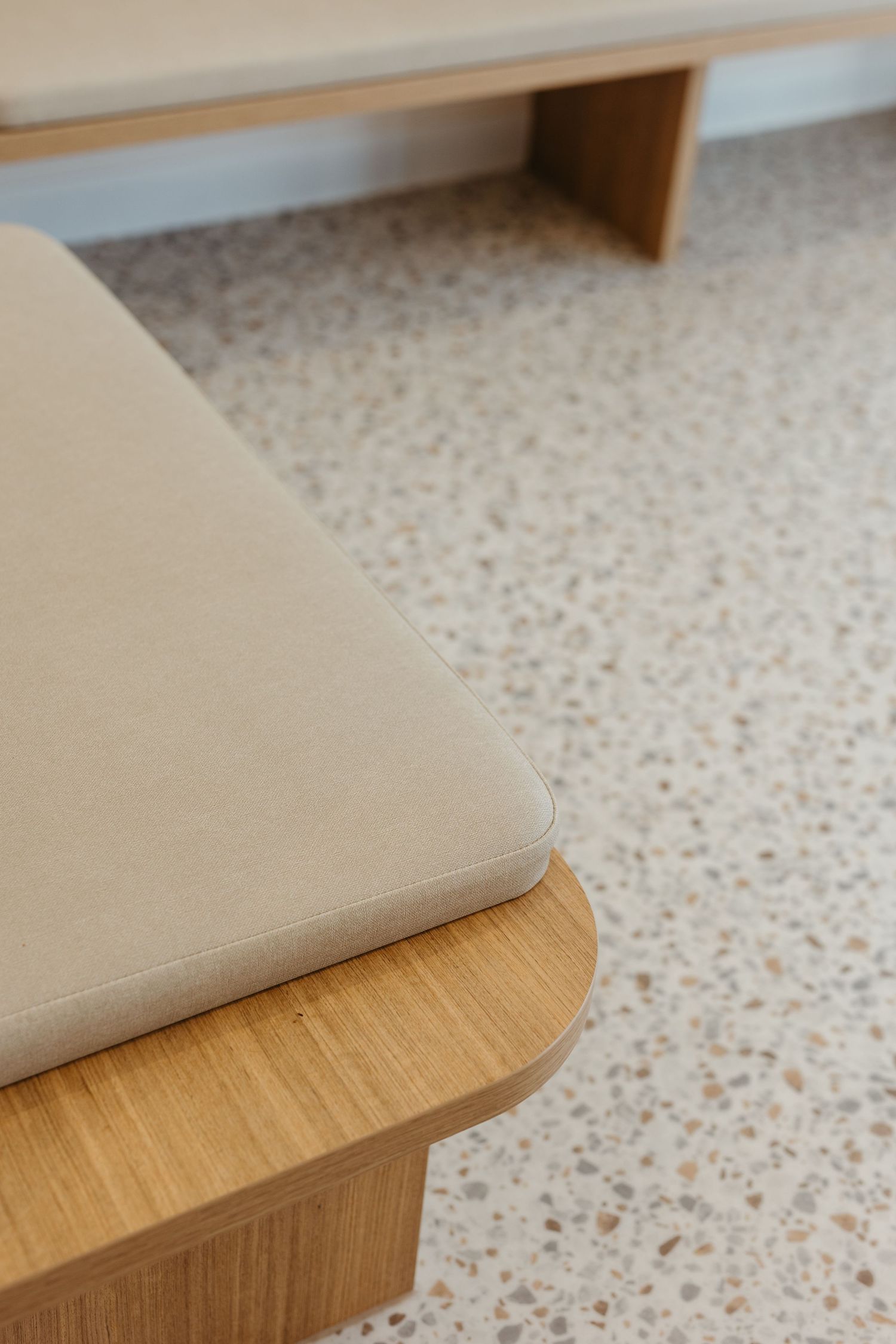 Close-up of a modern wooden bench with beige cushion on terrazzo floor.
