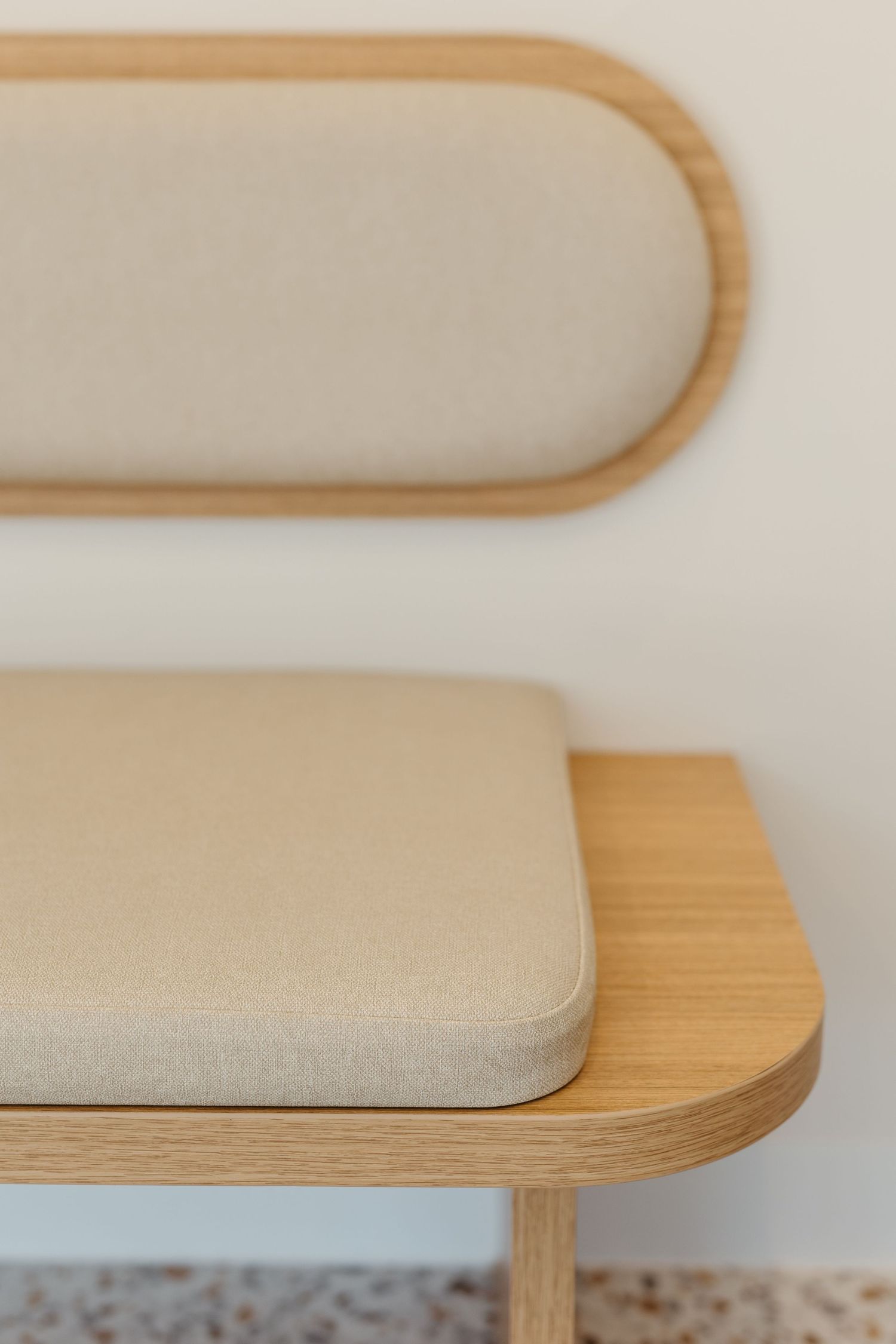 Close-up of a modern wooden bench with rounded upholstered backrest and cushioned seat in neutral beige fabric.