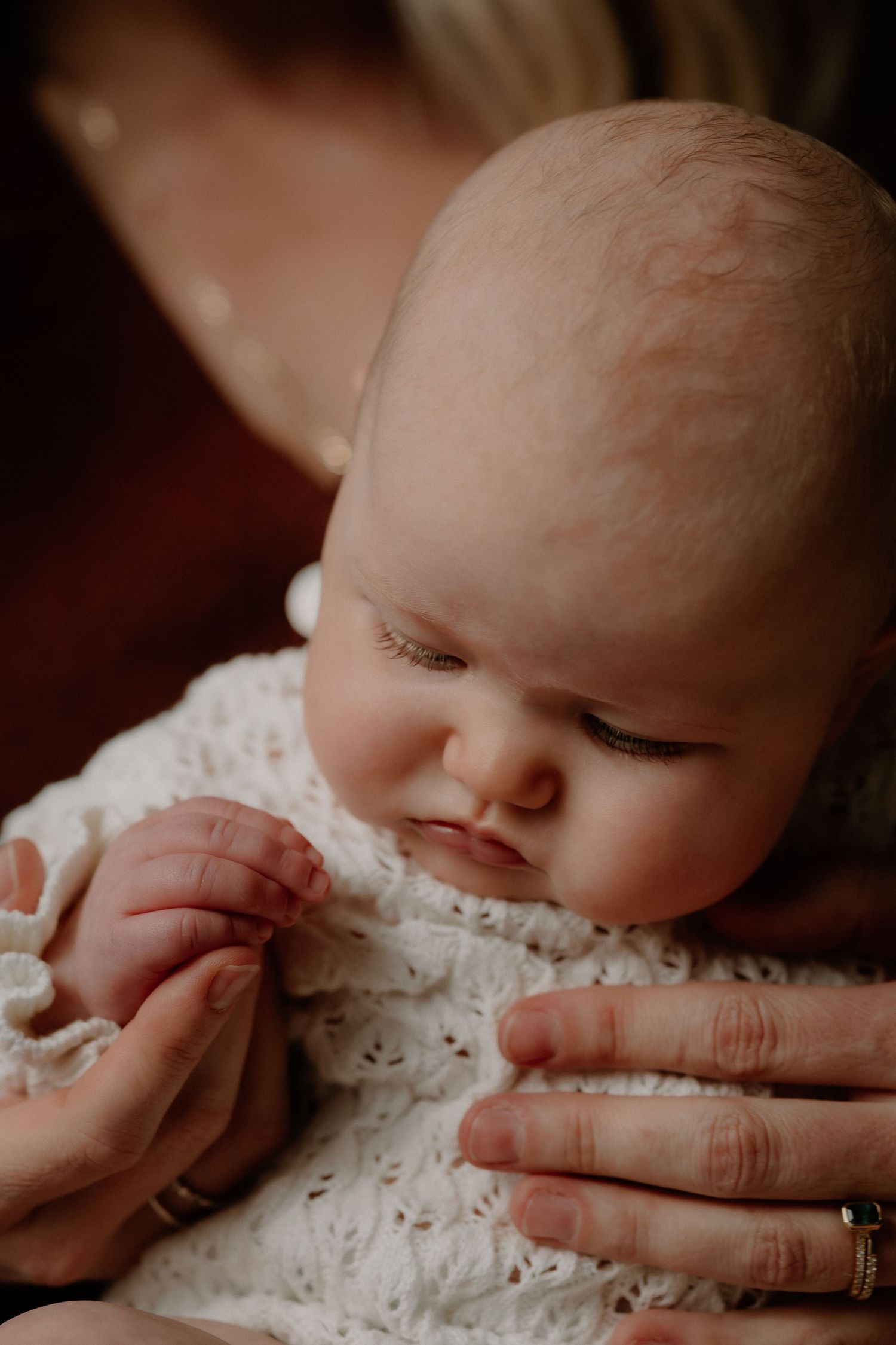 A newborn baby in a white lace outfit being cradled gently in adult hands.