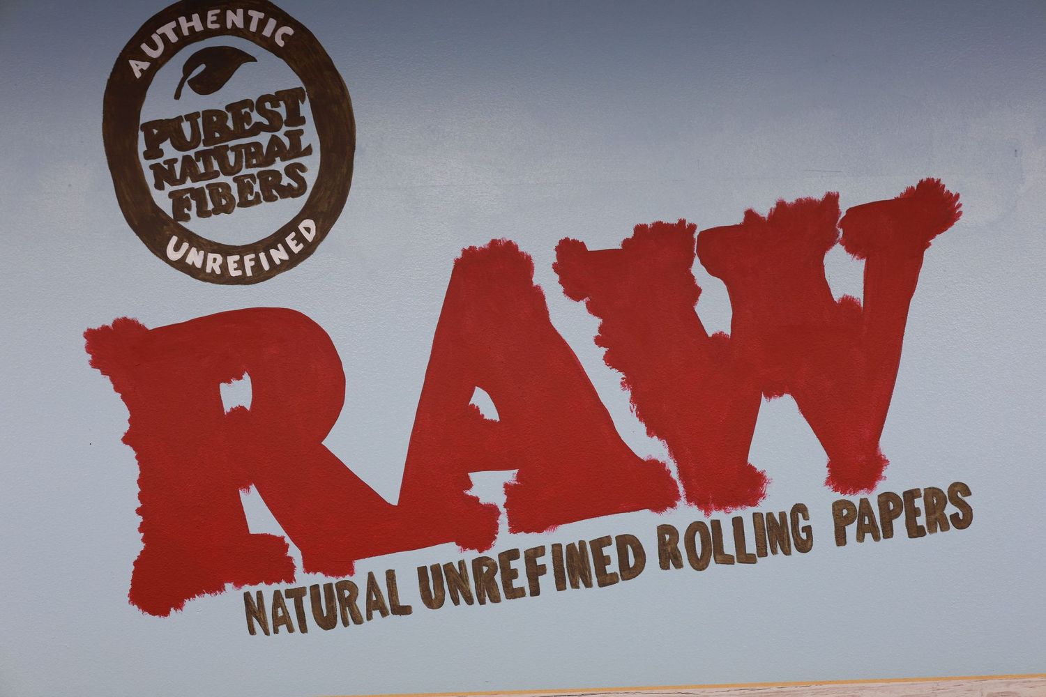 RAW Natural Unrefined Rolling Papers logo sign with Purest Natural Fibers branding on a tan background.