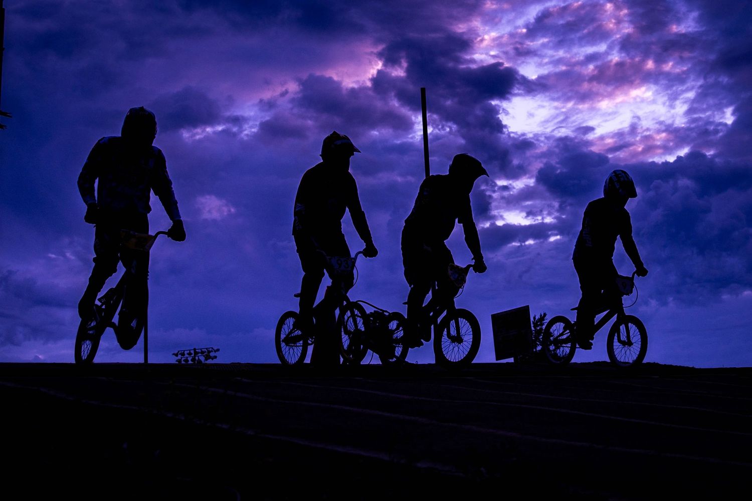 BMX rider performs a daring jump over a person lying on a dirt track while spectators watch at an outdoor cycling event.