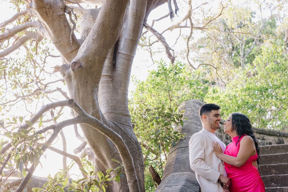 Couple embracing romantically under a large tropical tree on stone steps in a lush outdoor setting.
