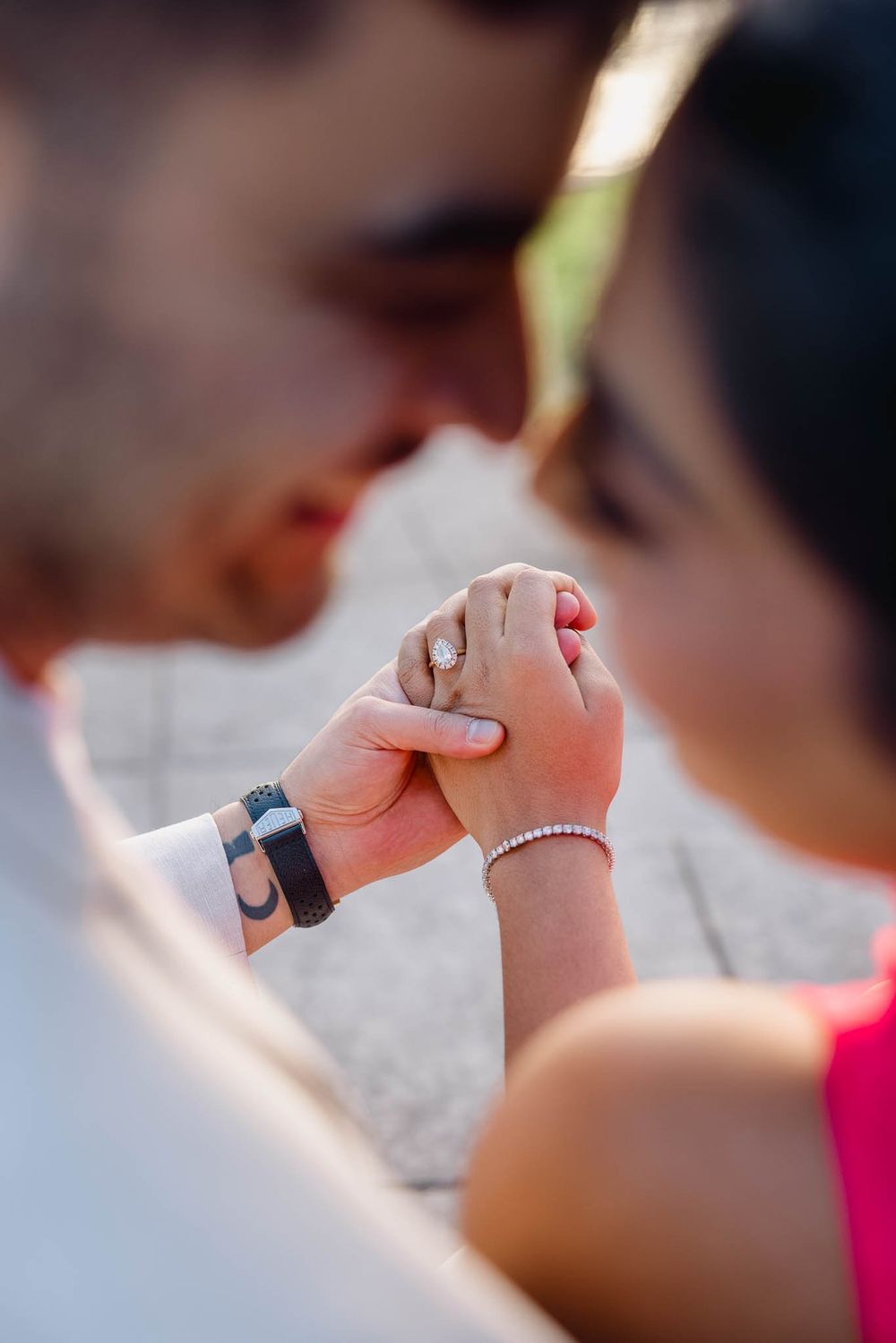 Close-up of an engaged couple holding hands, showcasing a diamond engagement ring and pearl bracelet.