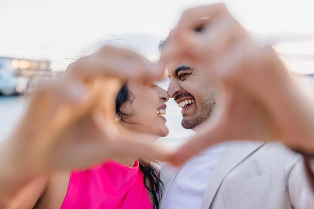 Couple making a heart shape with their hands while smiling at each other outdoors.
