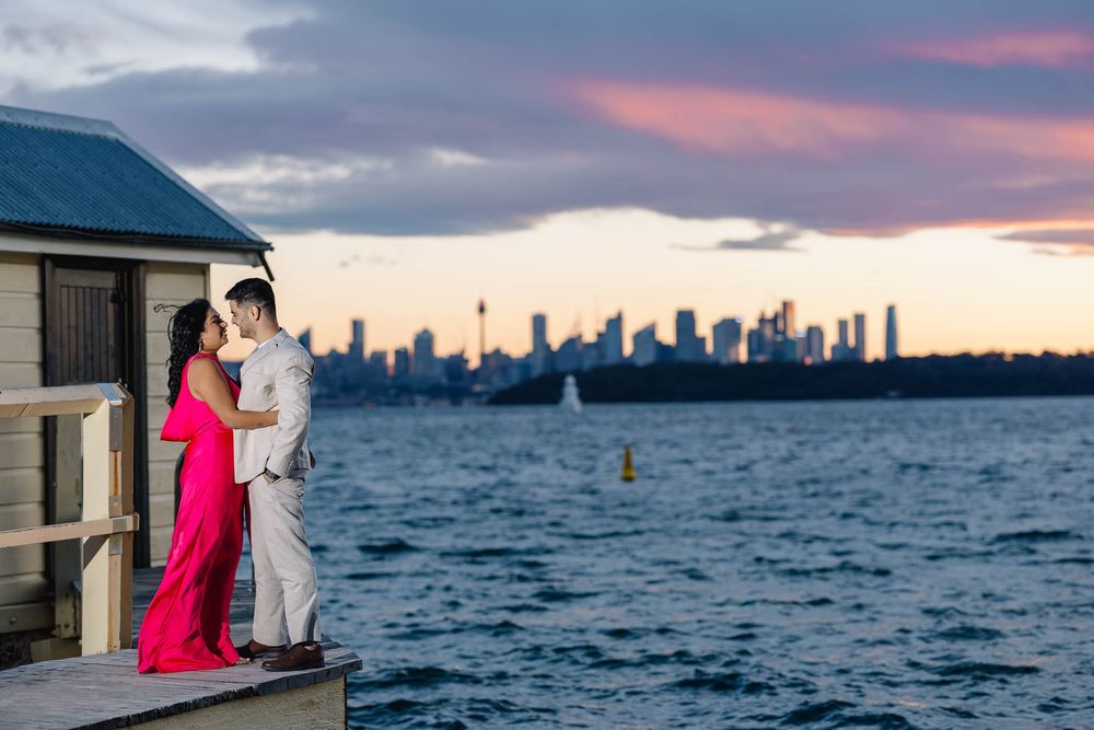 Romantic couple kissing on dock at sunset with stunning Sydney city skyline behind them.