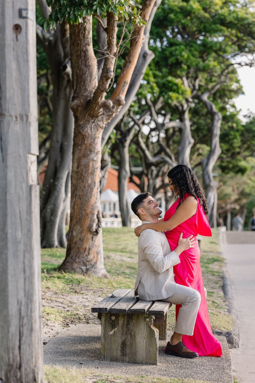 Couple in elegant attire sharing a romantic moment on a park bench surrounded by trees.