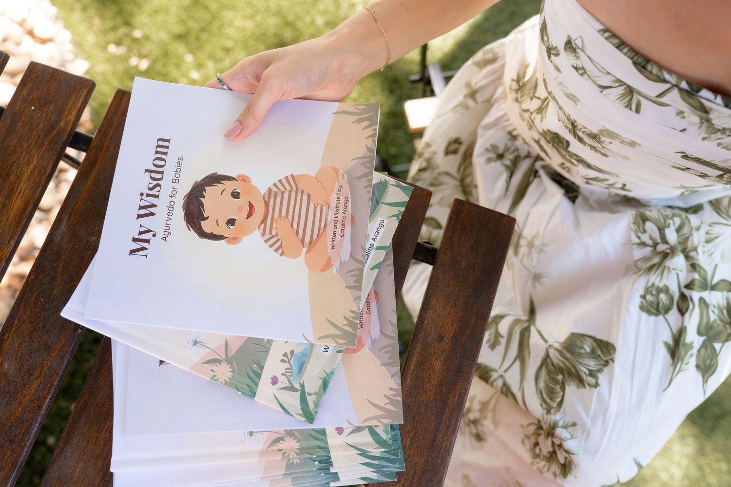 Person holding a My Wisdom children's book with illustrated cover on a wooden bench outdoors.